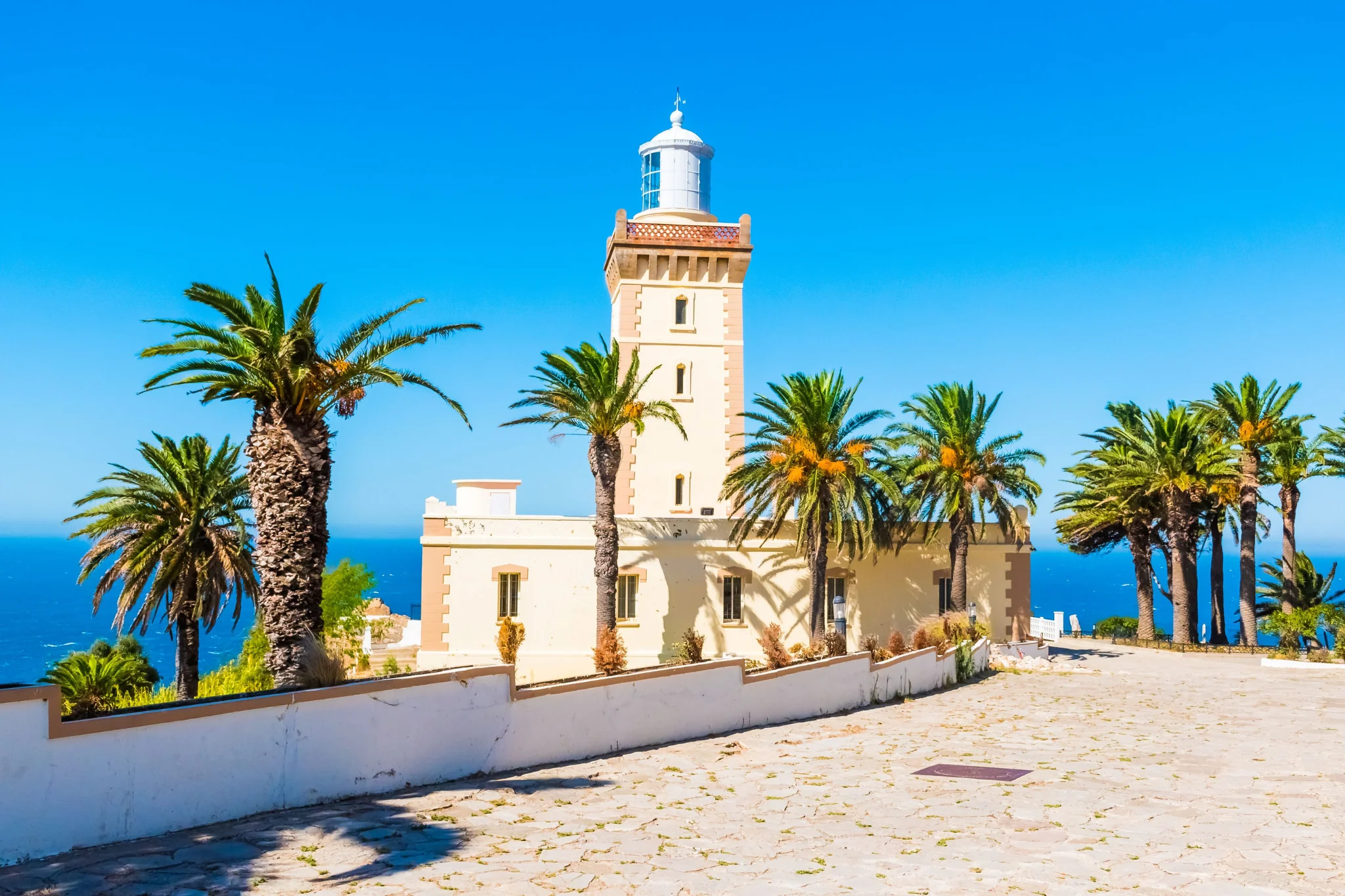 Phare jaune et blanc entouré de palmiers sous un ciel bleu.