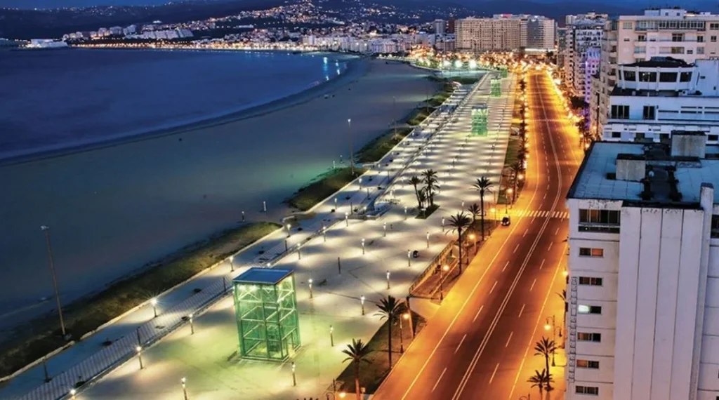 Avenue côtière illuminée de nuit longeant une grande plage.