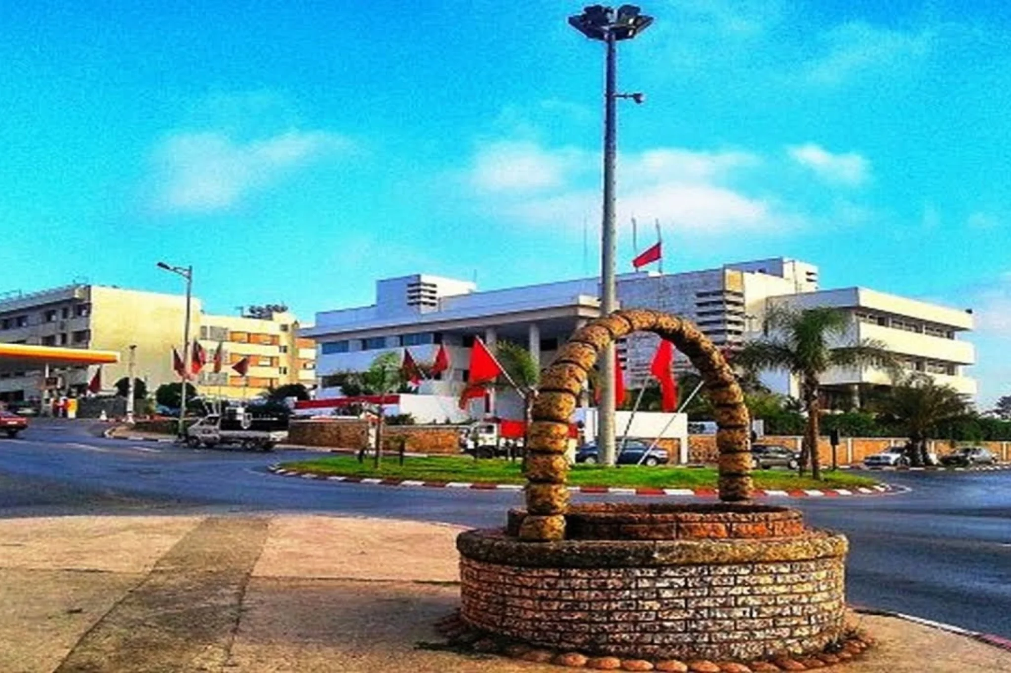 Fontaine en pierre devant un bâtiment blanc orné de drapeaux marocaine.