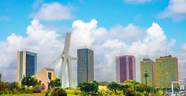 Vue panoramique du quartier des affaires du Plateau à Abidjan, mettant en valeur le pont Alassane Ouattara et les gratte-ciel modernes sous un ciel bleu parsemé de nuages blancs.