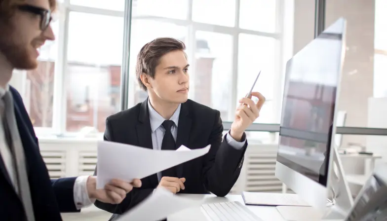 Deux professionnels analysent des documents financiers devant un écran